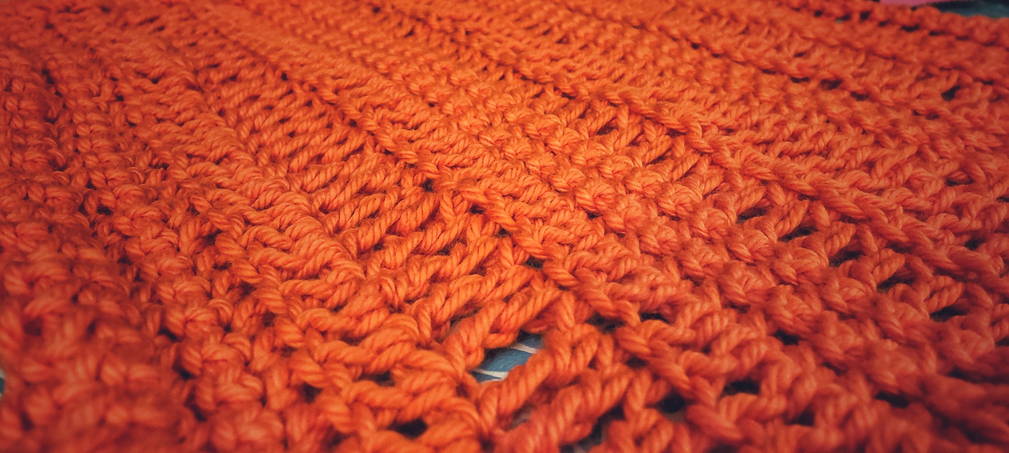a side view of a hand-crocheted washcloth in orange cotton yarn, showing off the stitch definition