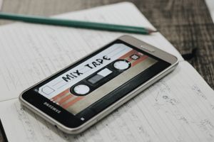 a modern Samsung smart phone sitting top of a notebook. There is an image on the phone’s screen that looks like a vintage cassette tape, with a label reading: Mix Tape